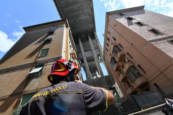 Пожарный смотрит на близлежащие здания из-под частично обрушенного моста Моранди в Генуе, Италия, 16 августа 2018 года