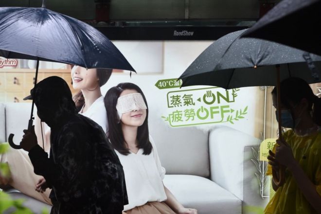 People walk past an advertisement as they take part in a rainy protest march from the Tsim Sha Tsui district of Hong Kong on October 6, 2019. - A Hong Kong judge on October 6 rejected a challenge to an emergency law criminalising protesters wearing face masks as democracy activists hit the streets again in defiance of the ban despite half the city's subway stations remaining closed.