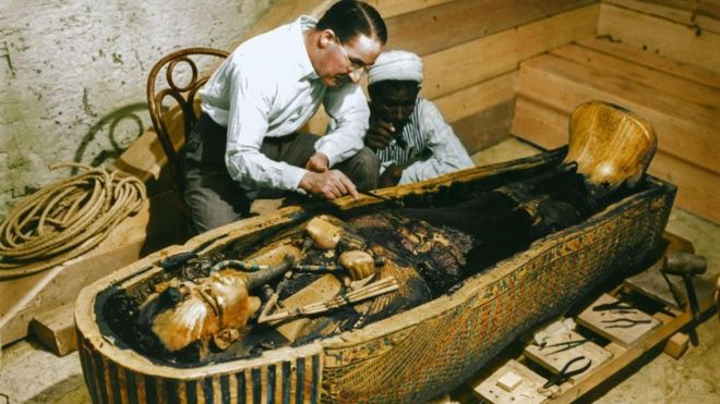 Arqueólogo Howard Carter e um trabalhador egípcio examinam um caixão feito de ouro maciço dentro da tumba