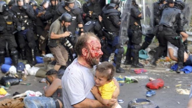 An injured migrant carries a child during clashes with Hungarian police. Photo: 16 September 2015