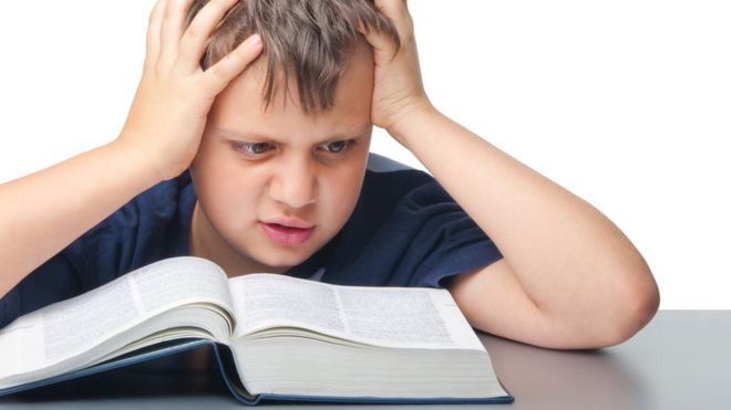 Un niño se toma la cabeza mientras lee el diccionario.