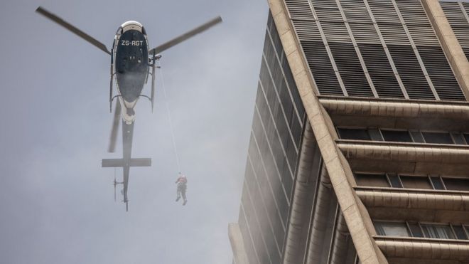 Человек, висящий на вертолете во время операции по спасению пойманного в ловушку пожарного - Йоханнесбург, Южная Африка