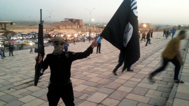 Боевик Исламского Государства Ирак и Левант (ИГИЛ) держит черное знамя и винтовку на улице в городе Мосул 23 июня 2014 года