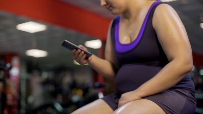 Женщина проверяет свой телефон в спортзале