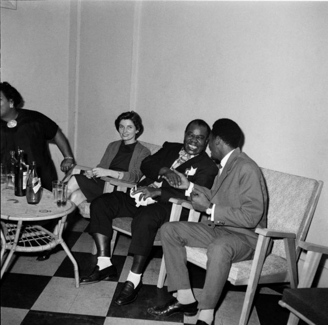 Le musicien de jazz américain Louis Armstrong (au milieu), tout souriant, serre la main d'un autre homme.