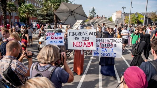 Imagem mostra mulheres segurando cartazes e sendo fotografadas em protesto realizado na cidade de Copenhague,no primeiro dia da implementação da proibição do véu no país