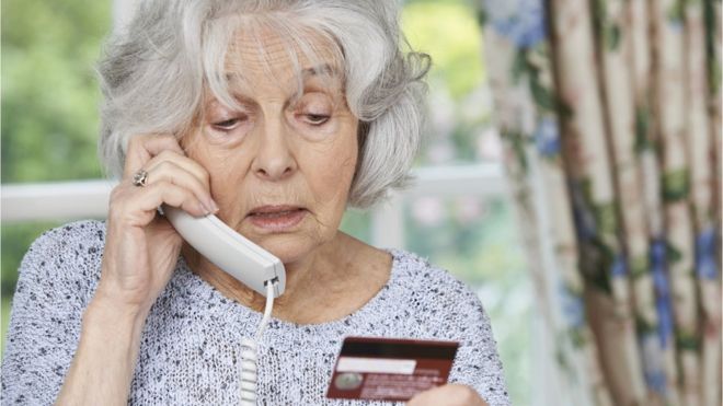 пожилая женщина разговаривает по телефону с кредитной картой
