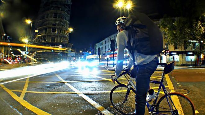 Čovek vozi bicikl u gradu, noć