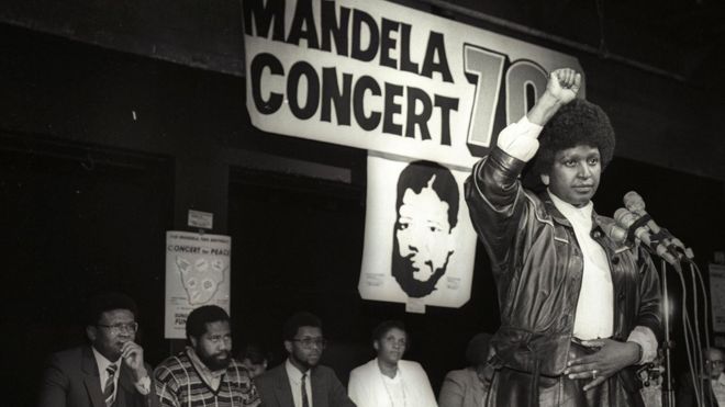 Винни Мандела поднимает кулак в черном силовом салюте после объявления о том, что в 1988 году состоится грандиозный поп-концерт, посвященный 70-летию ее мужа