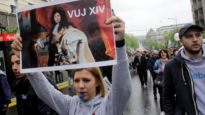Протестующие идут с сербскими флагами и держат изображение новоизбранного президента Сербии Александра Вучича в роли Людовика XIV, короля Франции в Белграде, Сербия, 8 апреля 2017 года