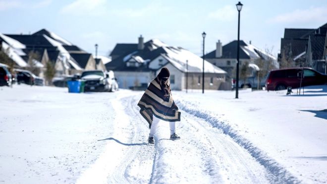 A man walks to his friend's home in a neighbourhood without electricity as snow covers the BlackHawk neighbourhood in Pflugerville, Texas, 15 February 2021