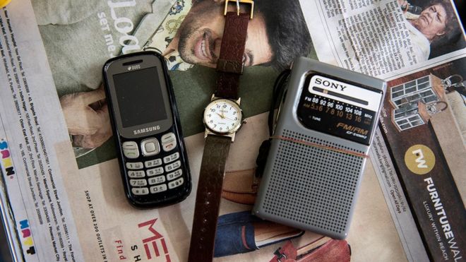 Мобильный телефон, часы и радиопередатчик, лежащие на газете в комнате в доме престарелых
