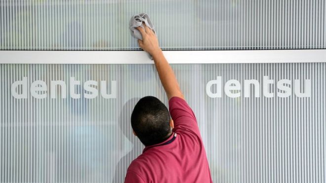 A man cleans a logo on a wall for Japan's Dentsu advertising agency