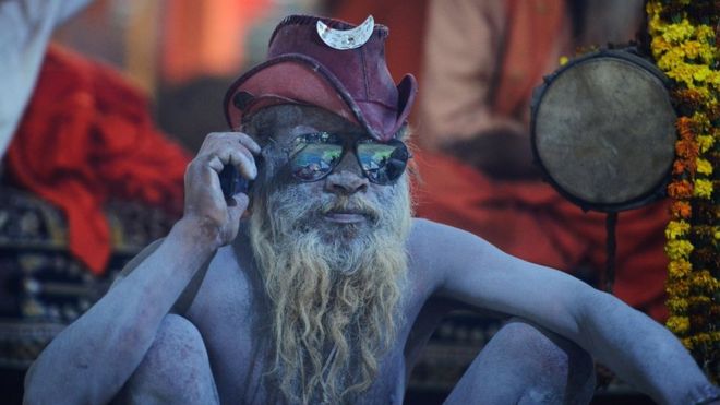Индийский садху (индуистский святой человек) сидит в своей палатке, когда он использует свой мобильный телефон во время фестиваля Кумбха-Мела в Аллахабаде 13 января 2019 года