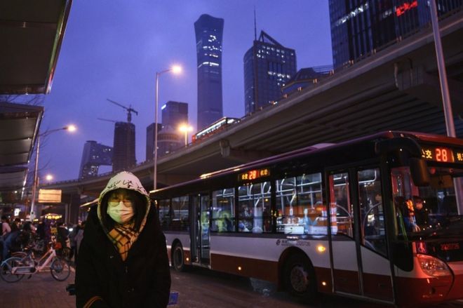 A Chinese office worker wears a protective mask as she waits to take a public bus after leaving work on 2 March 2020 in Beijing, China