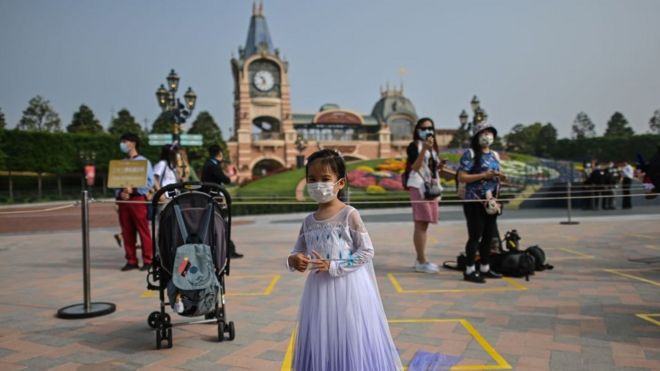 Девушка в маске ждет входа в парк развлечений Диснейленд в Шанхае 11 мая 2020 г.