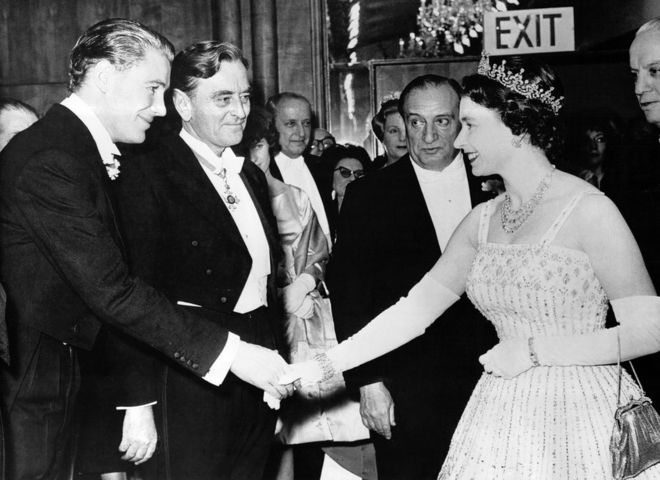 Королева приветствует кого-то на премьере фильма «Лоуренс Аравийский» на Лестер-сквер в Лондоне в 1962 году