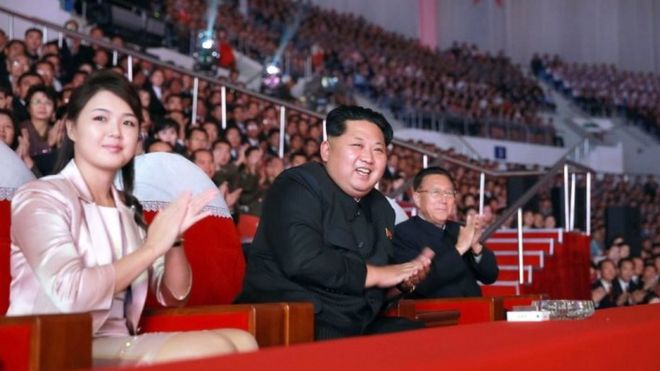 На этом недатированном файле, опубликованном официальным корейским центральным агентством новостей (KCNA) Северной Кореи 19 октября 2015 года, изображен северокорейский лидер Ким Чен Ын (C) в сопровождении своей жены Ри Сол Сю (слева).
