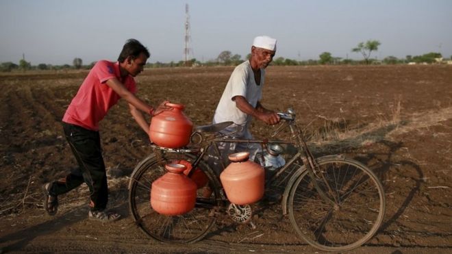 Жители проталкивают велосипед, наполненный контейнерами с водой, через поле в Латуре, Индия, 17 апреля 2016 года