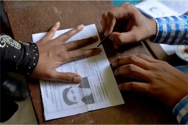 Индийский чиновник на выборах (R) наносит несмываемые чернила на палец избирателя, прежде чем она проголосует на выборах в Законодательное собрание штата Карнатака на избирательном участке в Бангалоре 12 мая 2018 года.