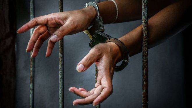 Руки в наручниках за тюремными решетками