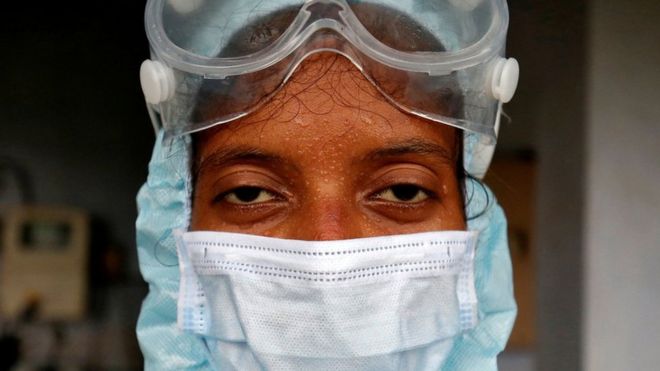 Beads of sweat run down the forehead of a healthcare worker wearing protective gear