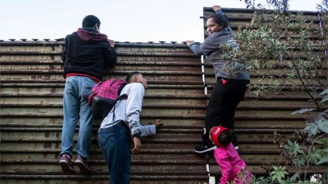 Гондурасские мигранты пытаются подняться на мексиканско-американский пограничный забор, чтобы пересечь округ Сан-Диего
