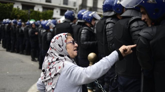 Mwanamke mkongwe wa Algerian akiongea na maafisa wa usalama waliokuwa wamewazingira waandamanaji wakati wa maandamano ya kupinga utawala katika mji mkuu Algiers Aprili 10, 2019. - Waandamanaji wa Algeria walnaendelea na maandamano hadi leo dhidi ya watawala waliopo madarakanilicha ya ahadi ya kiongozi wa taifa wa mpito ya kuendesha uchaguzi wa ''wazi'' wa urais kufuatia kujiuzulu kwa kiongozi mkongwe wa nchi hiyo Abdelaziz Bouteflika.