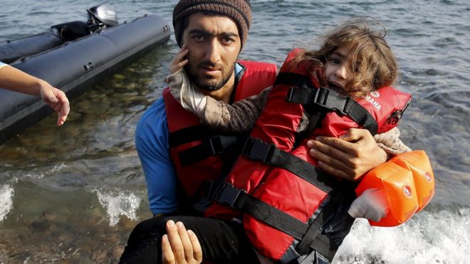 Сирийский беженец несет свою дочь по прибытии на пляж на греческом острове Лесбос