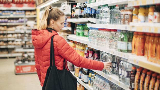 Женщина выбирает одноразовый напиток с полки супермаркета