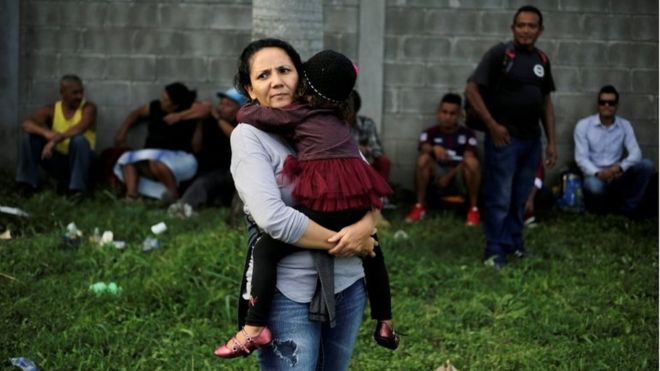 Гондурасская женщина несет свою дочь, когда они ждут, чтобы уехать с новым караваном мигрантов в Сан-Педро-Сула