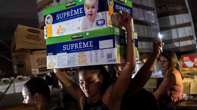 Женщина несет коробки с детскими подгузниками со склада, заполненного материалами, в Понсе, Пуэрто-Рико, 18 января 2020 года
