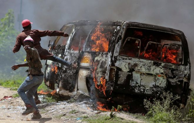 Сторонники кенийской оппозиции жестом возле горящего автомобиля в Эмбакаси, на окраине Найроби, Кения, 28 ноября