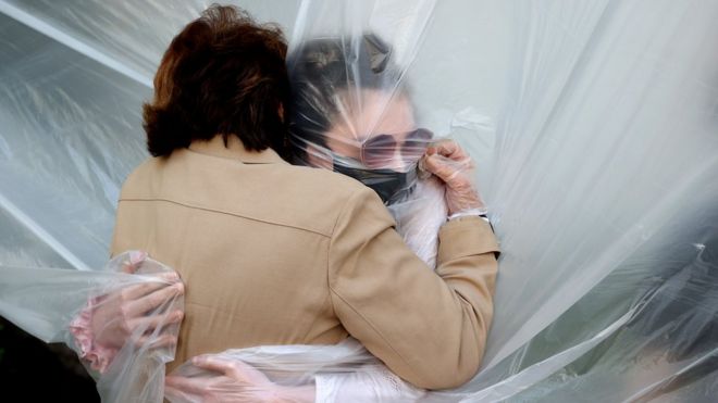 Olivia Grant (R) hugs her grandmother, Mary Grace Sileo through a plastic drop cloth hung up on a homemade clothes line during Memorial Day Weekend on May 24, 2020 in Wantagh, New York