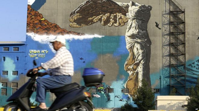 28 июня 2015 года мужчина проезжает на скутере мимо граффити с изображением Крылатой Победы Самофракии на стене старого здания в порту Пирей, недалеко от Афин. Происходит стабильный вывод средств из греческих банков
