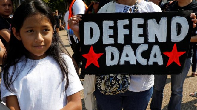 Una niña posa al lado de un cartel que dice: "Defendamos DACA", en inglés