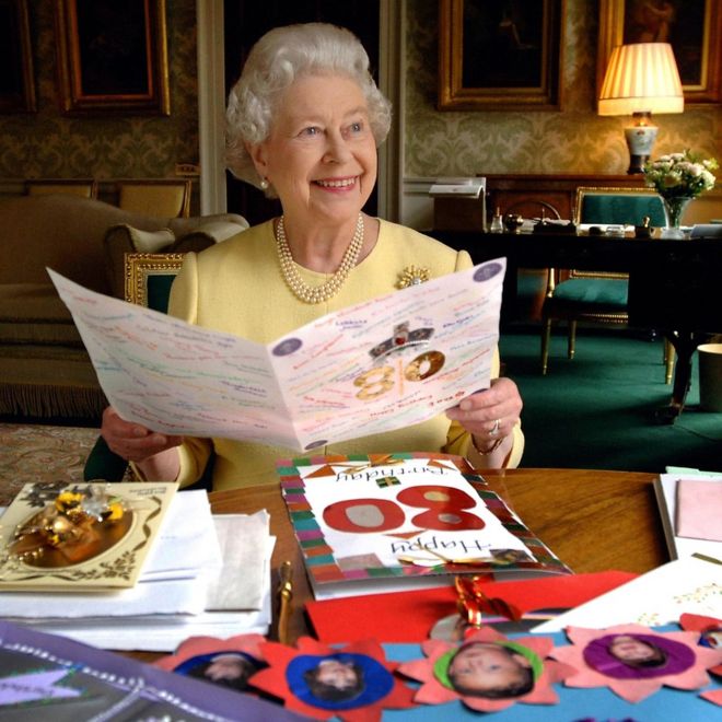 Королева Елизавета II сидит в зале ожидания в Букингемском дворце в Лондоне и смотрит на некоторые открытки, которые были отправлены ей на 80-летие