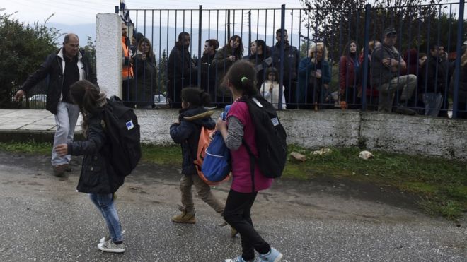 Девочки-беженцы смотрят на местных жителей, когда они проводят акцию протеста возле школы в греческой деревне Профитис, примерно в 35 километрах (22 милях) к востоку от Салоник, в понедельник, 10 октября 2016 г.