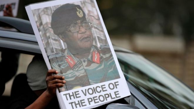Человек держит табличку с изображением командующего силами обороны Зимбабве Константина Чивенги, когда люди принимают участие в демонстрации с требованием отставки президента Зимбабве 18 ноября 2017 года в Хараре.