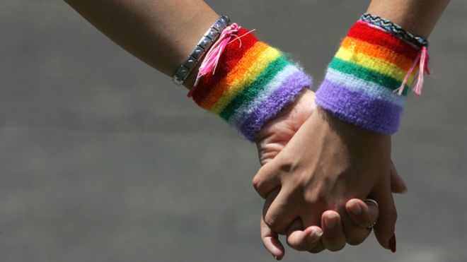 Dos mujeres con cintas arco iris se toman de las manos