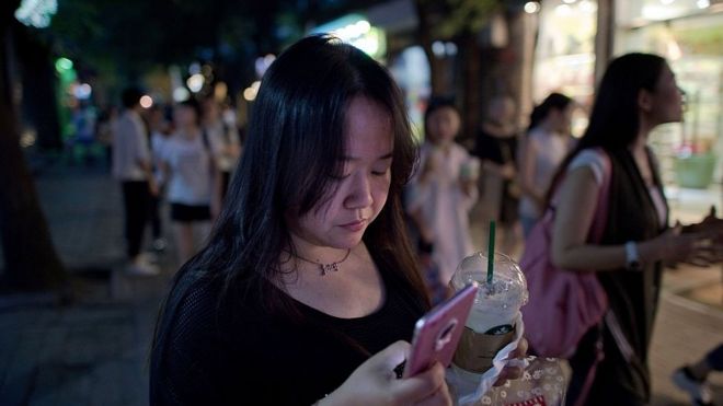 Китайская женщина использует свой смартфон, когда она идет по улице в Пекине.