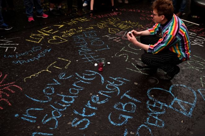 Женщина стоит на коленях среди граффити во время бдения в память о жертвах массового расстрела в ночном клубе для геев