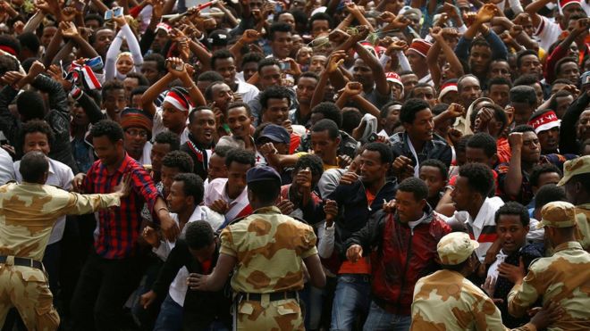 Демонстранты выкрикивают лозунги, высвечивая жест протеста Оромо во время Ирречи в Эфиопии - 5 октября 2016 года
