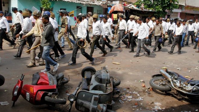 Индийские полицейские в штатском проходят мимо транспортных средств, поврежденных во время столкновения между двумя группами в Ахмадабаде, Индия, во вторник, 25 августа 2015 года.