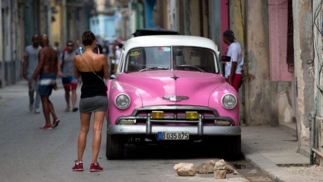 Молодая женщина фотографирует старинный автомобиль на улице в Гаване, Куба (20 марта 2016 года)
