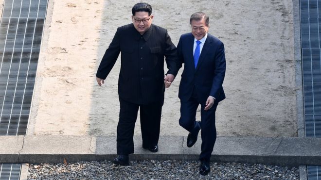 Лидер Северной Кореи Ким Чен Ун (слева) берет на себя руки президента Южной Кореи Мун Чжэ-ин (справа), когда они пересекают военную демаркационную линию на северную сторону после встречи на межкорейском саммите 27 апреля 2018 года в Панмунжоме, юг. Корея