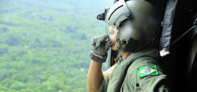 Militar olha da janela de aeronave sobre floresta na Amazônia