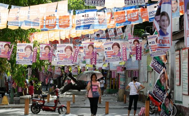 Женщина под зонтиком ходит под предвыборными плакатами, висящими через улицу в Тондо, Манила, 5 мая
