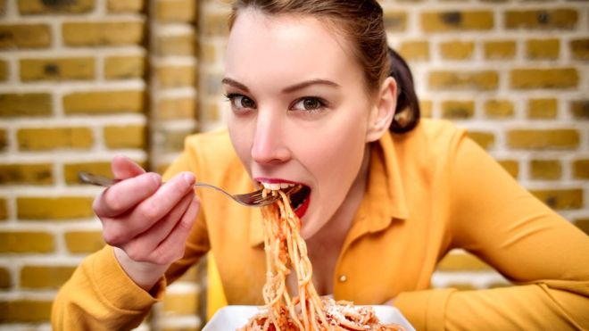 Mujer joven comiendo un plato de pasta en primer plano.
