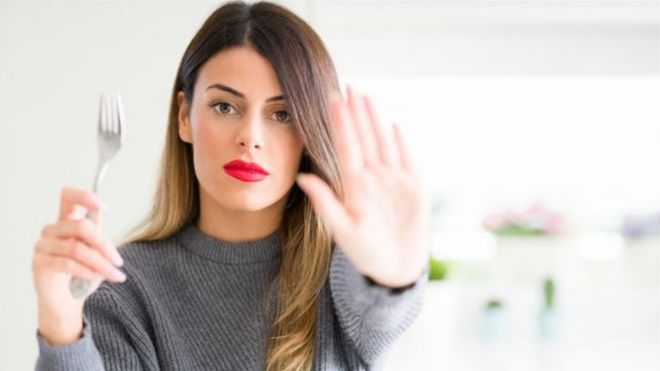 Mulher com garfo numa mão e fazendo sinal de pare com a outra